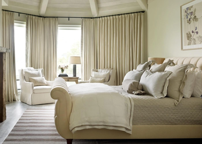 Cream pleated curtains in a luxurious, neutral-toned bedroom with a chaise lounge bed.