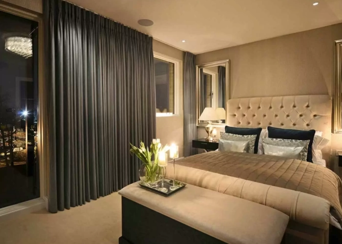 Dubai bedroom with floor-to-ceiling grey curtains, a beige tufted bed, and modern lighting.