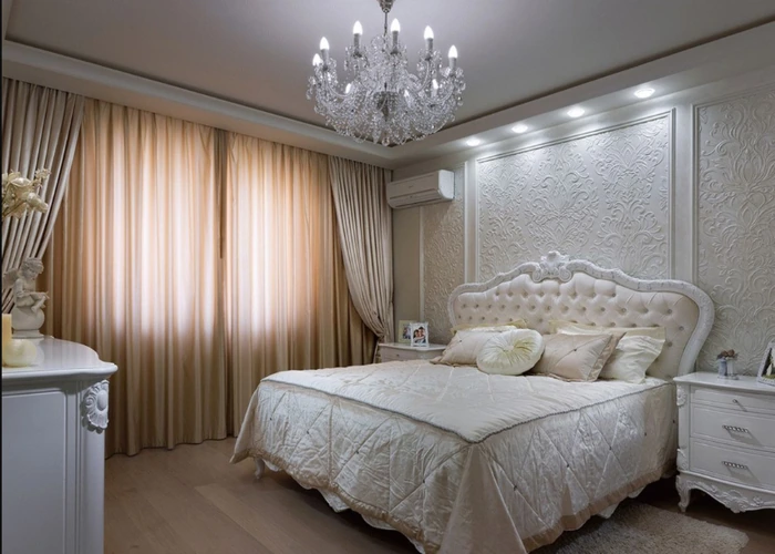 Elegant Dubai bedroom featuring cream curtains, a crystal chandelier, and a white tufted bed.