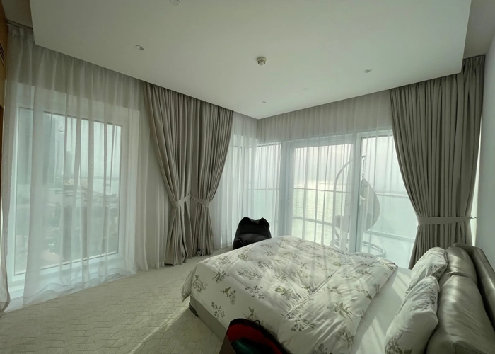 Large bedroom in Dubai with grey and white curtains and a view of the sea.