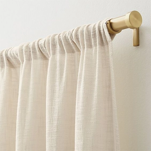 cream-colored, textured rod pocket curtain hanging on a matte gold curtain rod.
