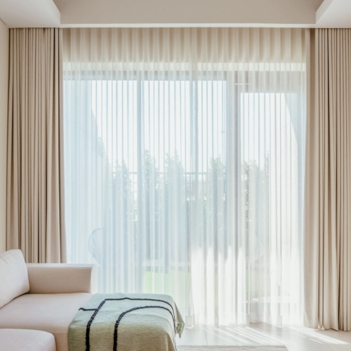 large window with a double curtain system, featuring beige, floor-length curtains on the outside and a sheer, white wave-style curtain in the middle.