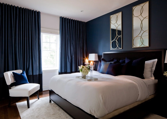 luxurious bedroom with deep blue walls, dark blue curtains, and a large bed with white linens.