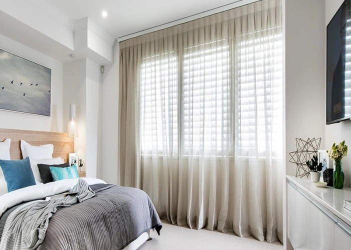 modern bedroom with sheer beige curtains and plantation shutters.