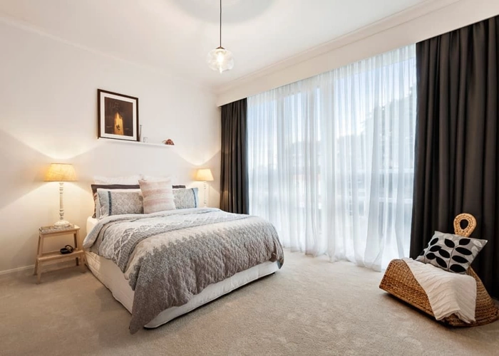 modern bedroom with white walls, a large bed, and sheer white curtains with dark-colored drapes.