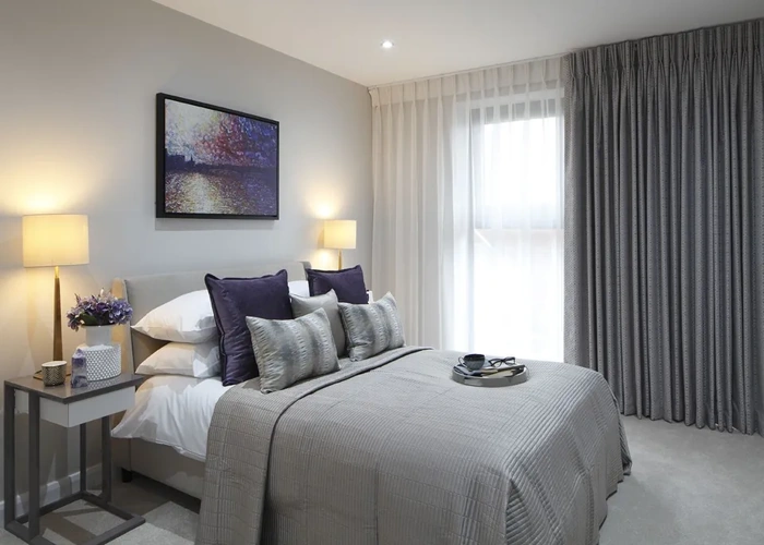 neutral bedroom with light gray walls, a bed with a gray blanket, and two sets of curtains.